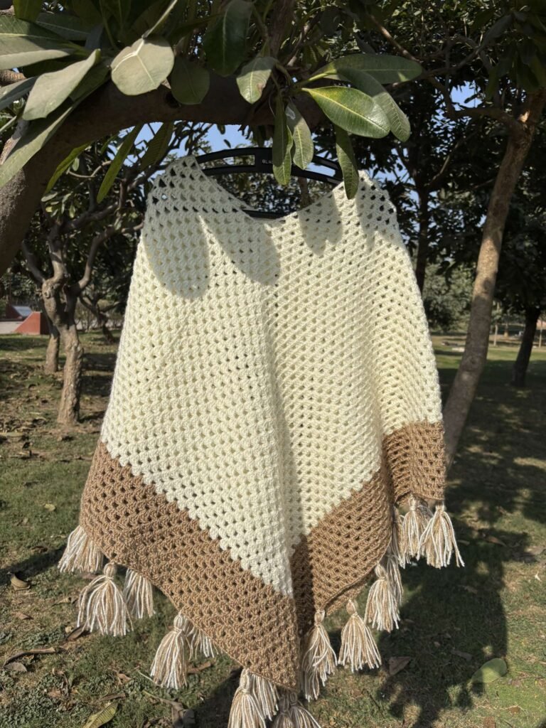 "A handmade crochet poncho made from soft, cozy wool, featuring intricate patterns and a loose, flowing design. The poncho has a textured knit, with fringe detailing along the hem. It is a warm, neutral color, ideal for cooler weather and can be worn casually or for a stylish, bohemian look."